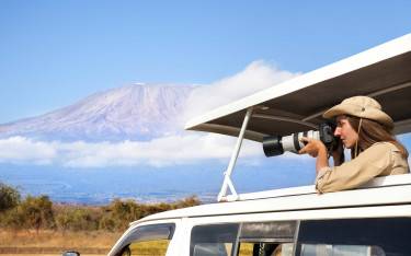 Safari-goer photographing from a vehicle with Mt Kilimanjaro in the background