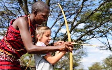 Maasai teaching girl to shoot a bow and arrow