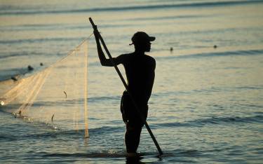 Thumbnail of Fisher walking into the sea with a net at sunrise